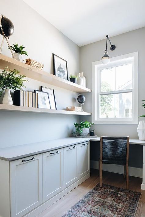 Blond wooden shelves are styled and stacked over a built-in l-shaped desk boasting white shaker cabinets and a gray desk top seating a black rope chair. Coastal Home Office, Coastal Office, Working Room, Modern Coastal Home, House Move, Modern Farmhouse Home, Drop Zone, School Room, Office Bar