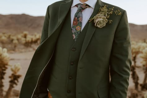 Close up photo of groom's green suit, floral tie and succulent boutonnière. Evergreen Suit Wedding, Eclectic Groom Attire, Men’s Garden Wedding Attire, Fall Wedding Tux Groom Attire Green, Boho Male Wedding Attire, Desert Wedding Groom Attire, Earthy Groom Attire, Bridesman Outfits Green, Green And Brown Groom Suit