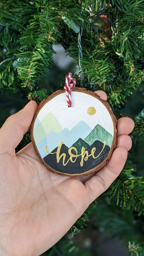 Bring a touch of natural beauty to your holiday decor with our Mountains Ornament Christmas Decoration, with a Hand painted hope text and mountains illustration, it is painted directly on a rustic wood slice.  This piece makes a thoughtful gift for nature lovers, art enthusiasts, or anyone who holds hope close to their heart. Order your Mountain Scene Christmas Ornament today and capture the spirit of the season in a way that's as unique and special as your own family traditions. Perfect as a stocking stuffer, secret santa, or as a gift tag ( text customized ) or heartfelt keepsake to cherish for years. - Hand painted Christmas ornament on wood slice - SIZE: ~3 in - word can be customized ( inquire in a DM ) Hiking Ornaments Diy, Mountain Ornament Diy, Painted Wood Discs, Wood Coasters Diy Painted Christmas, Diy Painted Wood Slice Ornaments, Diy Painted Ornaments Wood, Painted Wood Circles, Wood Burned Christmas Ornaments, Wood Slice Ornament Kids