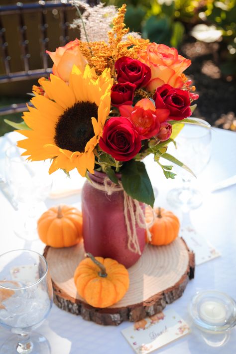 These outdoor fall wedding reception centerpieces included bright sunflowers, red roses, and other seasonal flowers alongside mini pumpkins and rustic wood pieces. This photo was taken by Megan Leigh Photography at one of our real fall weddings located at @josephamblerinn. Fall Wedding Centerpieces Sunflowers, Fall Bridal Centerpieces, Pumpkin And Sunflower Wedding Fall Decorating, Fall Wedding Decor With Sunflowers, October Wedding Sunflowers, Sunflower And Rose Centerpieces Diy, Pumpkin Sunflower Centerpiece, Fall Centerpiece With Sunflowers, Sunflower Red Rose Wedding Decor