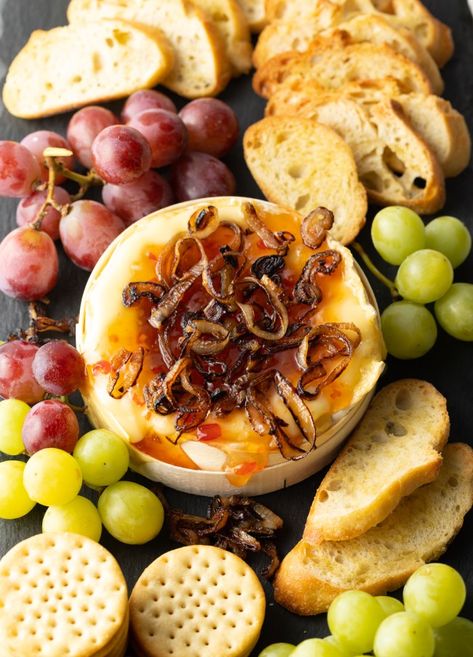 Top down view baked Camembert topped with sweet chili sauce and sauteed shallots. It is on a platter and surrounded by red and green grapes, crackers, and baguette slices. Recipe Using Brie Cheese, Baked Camembert Recipe, Camembert Recipes, Baguette Slices, Top Down View, Red Pepper Jelly, Sweet Appetizer, Impressive Appetizers, Baked Camembert