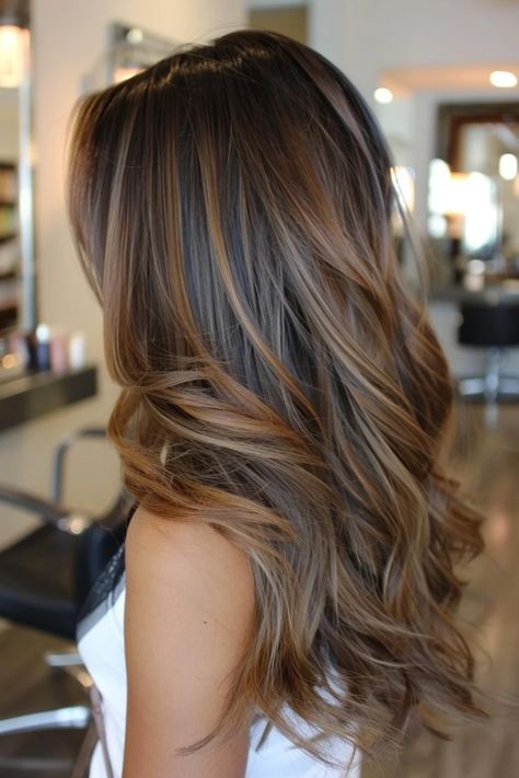 Woman with long, wavy hair featuring a brown balayage hairstyle in a modern salon. Medium Length Fall Hair Color Brunettes, Dark Brown Hair W Highlights, Long Hair Brown Balayage, Shoulder Length Dark Hair With Highlights, Medium Length Haircut Brown Hair, Brunette Hair Lowlights, Winter Balayage Brunettes, Brunette Hair Medium, Dimensional Brunette Highlights