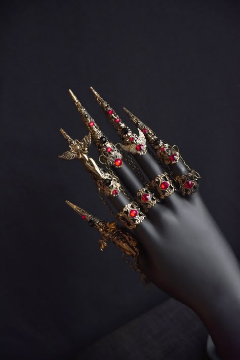 Beautiful gothic claw rings will be a great addition to your look. The photo shows a set of claws and medium rings in old gold color. The claws are decorated with small swords with wings and black and red rhinestones. The middle rings are attached to the claws with small chains.  The set includes 5 long claws and 4 medium rings Suitable for small and medium fingers. Not suitable for very wide fingers Claw rinds is available in different colors (see last photo). Finger Chain Ring, Red And Gold Accessories, Finger Claw Jewelry, Finger Claws, Hand Armor, Claw Rings, Brass Knuckle, Claw Ring, Claw Nails