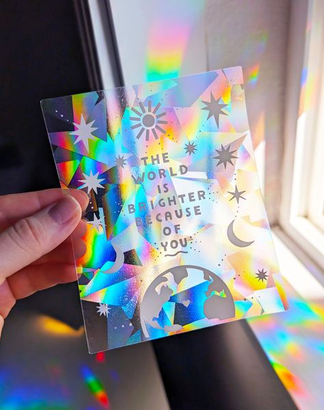 "The world is brighter because of you" ️  Featuring our original illustration, this sweet celestial suncatcher sticker makes a really beautiful gift for friends & loved ones! Suncatcher Decal Size: 4" x 5", Printed in White or Indigo ink on our gorgeous rainbow suncatcher prismatic film! Directions: Apply your new suncatcher decal to a window with * direct * sunlight (this is really important!) & watch vibrant rainbows bathe your space!  When bright direct sunlight hits the surface, our radial s Color Window Film, How To Make Suncatcher Stickers, Diy Suncatcher Sticker, Window Rainbow Prism, Sun Catcher Window Sticker, Suncatcher Sticker, Rainbow Maker, Diy Stickers, Window Stickers