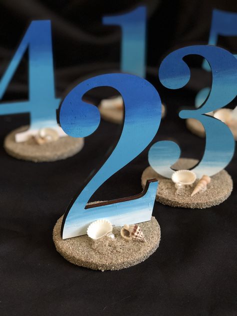 Custom designed beach themed table numbers. Ordered blank table numbers from Etsy and painted my own! Added some sand, a few shells and a pearl. They're perfect. Wedding Sea Theme, Table Numbers Beach Wedding, Table Numbers For Beach Wedding, Shell Table Number, Beachy Wedding Table Numbers, Sea Shell Wedding Table Decor, Buoy Table Numbers Wedding, Beach Theme Table Numbers, Nautical Table Numbers