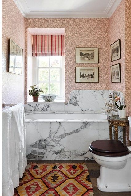 Interior designer Amanda Hornby has used 'Vermicule' wallpaper from Pierre Frey in the bathroom, which contrasts with the marble bath surround and swooping curved splashback, sourced from a quarry that was reopened 20 years ago when the marble in the Hall of Mirrors at Versailles was being restored, 'I love its funky psychedelic orange and red veins,' says Amanda.    Taken from the August 2015 issue of House & Garden. Bath Surround, Marble Bathtub, Small Bathroom Layout, Iron Console Table, Painted Cupboards, Add Storage, Marble Bath, Small Bathroom Design, Bathroom Layout