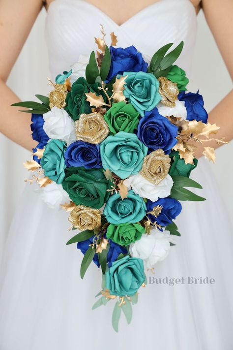 This lovely assortment of royal blue, emerald green, teal and white roses is bound to turn heads on your wedding day. This lovely cascading brides’ bouquet from the is an absolutely breathtaking arrangement for any bride to be, in any season. Gold accents and greenery and gold glitter roses complete the look and add a delicate realism to this beautiful bouquet. This bouquet is 10” wide, 18” long, and is crafted by our in-house florists without using a foam base to anchor the flowers to the bouqu Emerald Green Blue And Gold Wedding, Royal Blue Emerald Green Wedding, Teal And Mint Green Wedding, Emerald Green And Royal Blue Wedding, Green And Royal Blue Wedding, Emerald Green Royal Blue Color Palette, Blue And Emerald Green Wedding, Emerald Green And Navy Blue Wedding Wedding Ceremony Decor, Royal Blue And Emerald Green Wedding