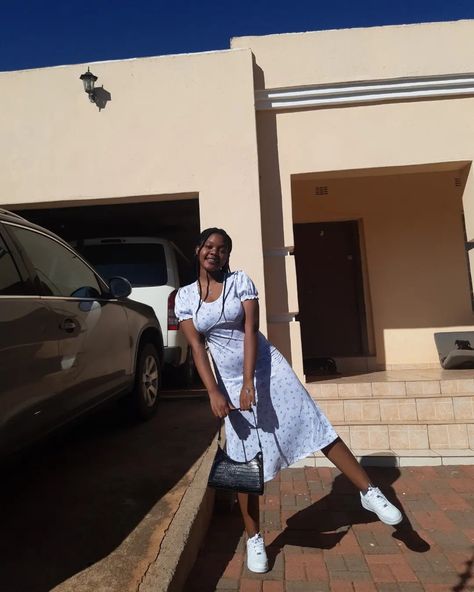 Girl in white dress with little florals, wearing white airforce 1s, holding a black shoulder bag with both arms while leg is extended. 2 Cars in the background, she is a woman of colour with braids. Af1 Outfit, Dress Cottagecore, Cottage Core, Braids, Cottage, Black, Plaits