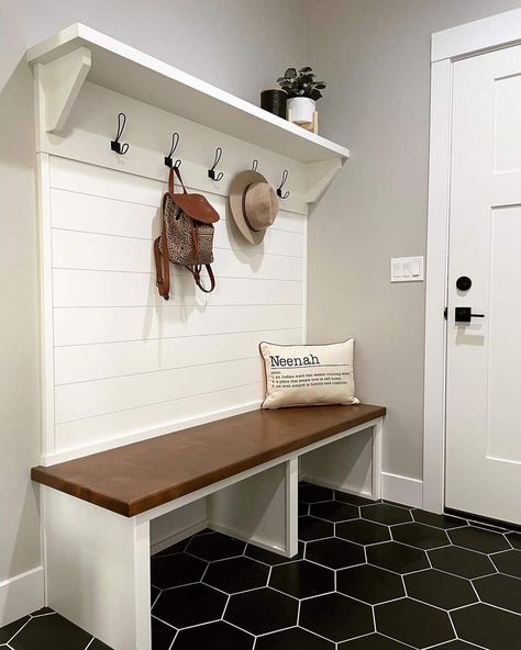 A two-toned white shiplap mudroom bench with black metal coat hooks is styled with greenery and tan décor. The bench stands on stunning black hexagon floor tiles in this gray entryway featuring a white door with black hardware. Butcher Block Mudroom Bench, Shiplap Mudroom Wall With Hooks, Shiplap In Mudroom, How To Build A Mudroom Bench, Mudroom Hooks And Bench, Entryway Hooks And Bench, Shiplap Mudroom Entryway, Mud Room Floor Ideas, Mud Room Benches