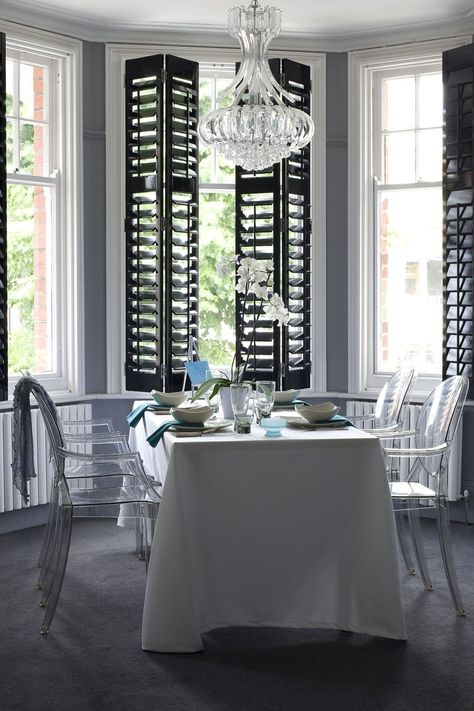 Mix up your monochrome scheme by opting for black gloss shutters over white. When combined with ghost dining chairs and a chic chandelier, the look is oh so glamorous.   Shutters from [link url="http://www.thecaliforniacompany.co.uk"]The California Company[/link]  [link url="http://www.houseandgarden.co.uk/homes/furnishings/lighting"]LIGHTING IDEAS WE LOVE[/link] Shutters Indoor, Bay Window Shutters, Indoor Shutters, Best Interior Design Websites, White Shutters, Interior Window Shutters, Black Shutters, Modern Blinds, Living Room Blinds