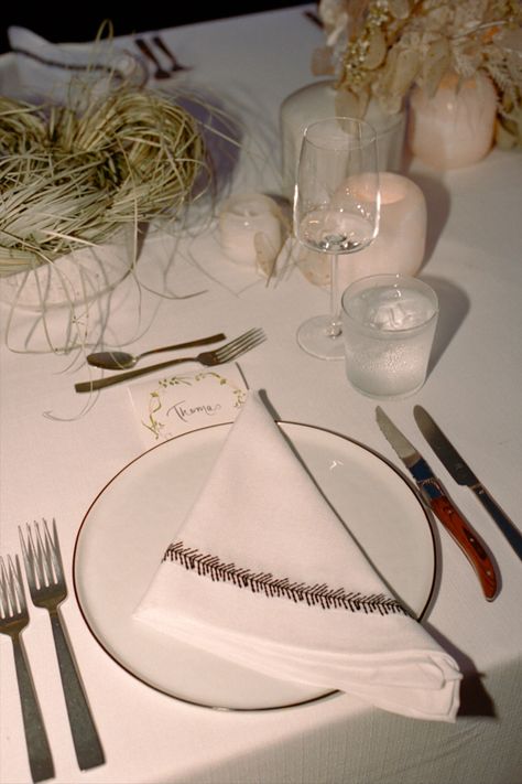 A table setting with a white plate, a white napkin, and a place card. There is a glass of water and a candle in the background. Minimalist Table Setting, Modern Wedding Table, Wedding Table Setting, Minimalist Table, Minimalist Tables, Event Branding, Fancy Party, Wedding Table Settings, Wedding Tablescapes