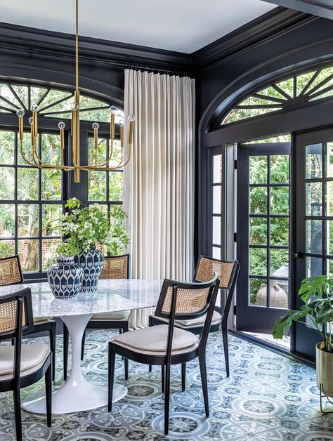 Previously a sunporch, the dining room already boasted patterned encaustic tile floors and a vintage-inspired brass chandelier by Generation Lighting. The design team enhanced the space by way of Benjamin Moore’s Mopboard Black and a marble-topped Stilnovo table surrounded by Four Hands cane chairs. Terracotta Design, Cane Dining Chair, Southern Homes, Luxe Interiors, Trends 2023, Elegant Dining, Upholstered Seating, Interior Design Services, Dining Room Decor