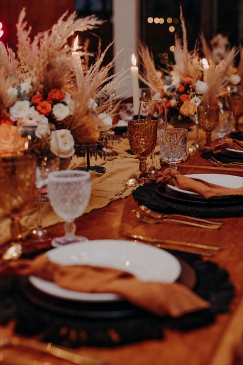 wooden table with black macrame charger, amber and white glass, gold cutlery, terracota napkin and pampas everywhere. Copper And Black Wedding Decor, Burnt Orange And Brown Wedding Decor, Burnt Orange Black And Gold Wedding, Orange Black And White Wedding, Amber And White Wedding, Black White Orange Wedding, Black And Orange Table Setting, Black And Amber Wedding, Rust And Black Wedding Decor