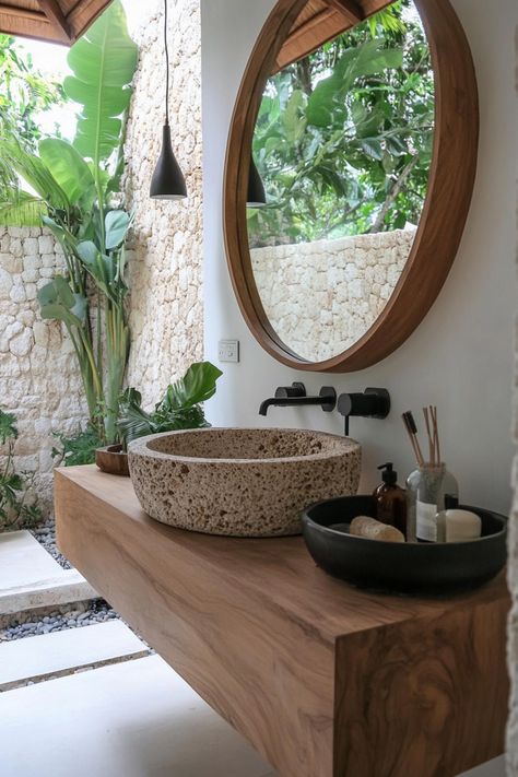 Rustic bathroom with a stone sink, wooden countertop, large round mirror, and stone walls, surrounded by lush greenery. Modern Desert Bathroom, Desert Bathroom, Organic Modern Bathroom, Bathroom Elegant, Sink Bowl, Modern Desert, Powder Room Decor, Black Countertops, Dark Academia Decor