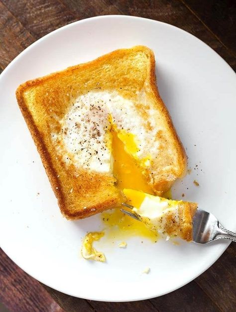 Egg in a Hole is a delicious piece of toast that has an egg soft cooked in the center, which has been cut out. This popular breakfast has many names, like Toad in a Hole, egg in a frame, egg in the basket, but this egg in toast recipe is delicious no matter what you call it! simplyhappyfoodie.com Dropped Eggs On Toast, Eggs In Bread Hole Recipes, Egg In A Hole Skillet, Bread With Egg In Middle, Egg In The Hole, Bread Factory, Simply Happy Foodie, Egg In A Hole, Brunch Spread