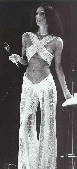 Cher, 1970s. White and sequin bell bottom pants with a criss cross top. 1970s Outfits, Cher 70s, Look Disco, 70s Mode, 70s Jumpsuit, Cher Outfits, Fashion 70s, Gene Kelly, Mae West