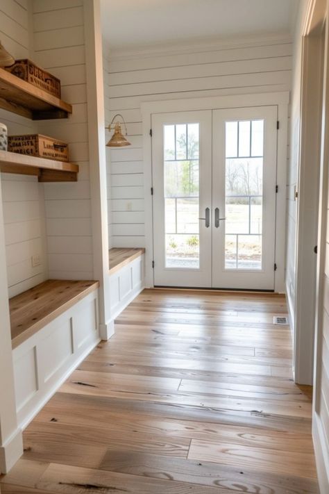 Bright entryway with wooden flooring, white shiplap walls, a built-in bench on the left, and double doors with glass panes letting in natural light. Farmhouse Cased Opening, Colorado Modern Farmhouse, White Farmhouse Interior Design, Rustic Flooring Ideas Farmhouse Style, Mudroom With Bathroom, Kitchen With Mudroom, Backdoor Mudroom, White Farmhouse Interior, House Design Farmhouse