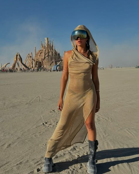 A golden vision against a monumental backdrop, this look flows with elegance and mystery. The shimmering hooded dress paired with futuristic goggles and sleek arm cuffs create a captivating fusion of desert warrior and celestial goddess 🏜️🌟 @kathimodelofficial 🔥🔥 Burning Man Fashion Woman Inspiration, Desert Glam Outfit, Futuristic Desert Fashion, Futuristic Festival Outfit, Dune Festival Outfit, Desert Festival Outfits, Burning Man Festival Women, Desert Costume, Burning Man Fashion Woman