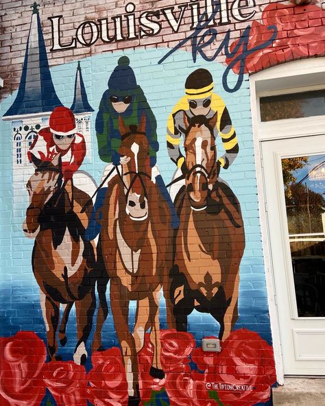 The image shows a custom mural painted on the back of an AirBnB. The mural is Kentucky-themed with three Derby horses racing among red roses. There are three jockeys wearing red, green and blue, and yellow and black. The background is light blue with a darker blue ombre at the bottom. The top of the mural says "Louisville, KY". The twin spires are behind a horse on the left of the mural painting. The mural is to the left of the back door of the AirBnB and there are red roses above the doorway. Airbnb Mural, Air Bnb Tips, Derby Horse, Custom Murals, Air B And B, Window Painting, Photo Op, Louisville Ky, School Colors