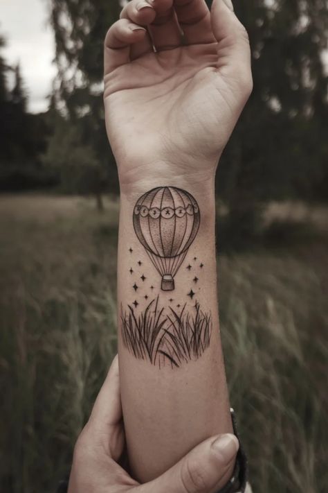 Hot air balloon tattoo above grass on forearm with hand holding wrist. Dainty Wrist Tattoo, Tattoos For Women Delicate, Women Tattoo Inspiration, Hot Air Balloon Tattoo, Air Balloon Tattoo, Tattoo Ideas For Females, Balloon Tattoo, Wrist Tattoo Ideas, Wrist Tattoos For Women