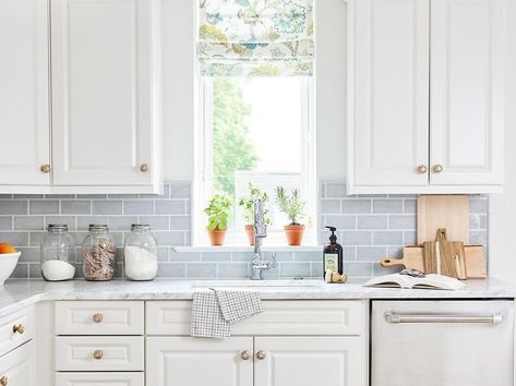 Light blue subway tiled backsplash accents white raised panel cabinets finished with brass knobs and marble countertops. Light Blue Subway Tile, Blue Subway Tile Backsplash, Light Blue Backsplash, Blue Backsplash Kitchen, Light Blue Tile, Blue Subway Tile, Raised Panel Cabinets, Marble Counters, Beach House Kitchen