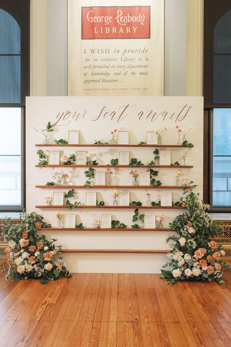 We transormed these shelves into a beautiful seating chart by incorporating lush flowers and thoughtful design. For this wedding at the George Peabody Library, we adorned a bookshelf with vibrant florals, creating a visually stunning and functional display. Each guest's seat was elegantly displayed among the blooms, adding an extra touch of beauty and personal charm to the space. Photo: L Hewitt Photo Wedding Wall Seating Chart, Wildflower Seating Chart, Garden Wedding Seating Chart, Picture Frame Seating Chart, Flower Seating Chart, Seating Chart Wall, Seating Chart Display, Wedding Seating Chart Display, George Peabody Library