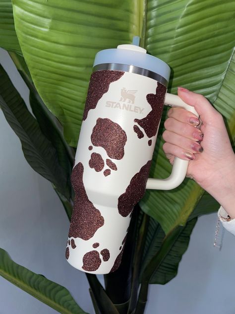 Hand-painted sparkly cow print Stanley tumbler  Genuine Stanley tumbler with many different size and color options! This product is hand-painted and the glitter is applied by hand, so each cup is unique!  A water resistant coating has been applied to the cup, but this product is NOT dishwasher safe as the heat from the dishwasher can eventually cause any coating to break down. Do NOT wash with any abrasive material. Gently wash by hand.  Returns and exchanges accepted within 7 days of delivery a Stanley Cup Cow Print, Cow Print Stanley Cup, Preppy Basket, Western Stanley, Cow Print Stuff, Cowgirl Cakes, Fancy Cup, Stanley Adventure, Stanley Cups