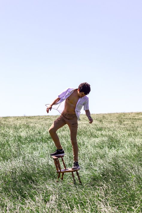 Boy balances on top of a chair, with an unbuttoned white shirt and beige cargo pants. He is in a green field, and blue skies are in the background. Farm Photoshoot Ideas Men, Man Photography Poses, Future Cowboy, Freedom Photography, Men Posing, Graduation Picture Ideas, Grass Fields, Photo Session Ideas, Male Models Poses