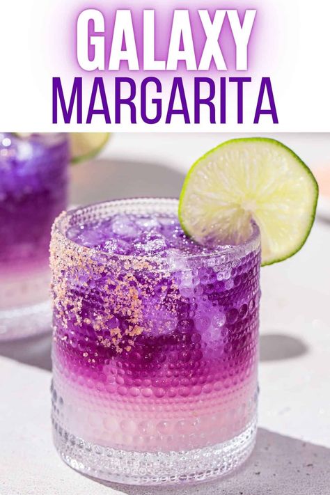 The Galaxy Margarita is as tasty as it is beautiful! Tequila that's naturally colored by butterfly pea flowers is layered on top of a Cointreau and lime base. Edible glitter takes it to the next level! It is a fun galactic spin on a classic margarita. This is the perfect margarita recipe for a girls night, bachelorette or just a night of stargazing! Butterfly Cannon Blue Tequila Recipes, Space Drinks Alcohol, Tequila Galaxy Cocktail, Purple Margarita Recipe Tequila, Birthday Margarita, Cotton Candy Margarita Recipe, Butterfly Pea Flower Margarita, Colored Cocktails, Butterfly Pea Cocktail Recipe