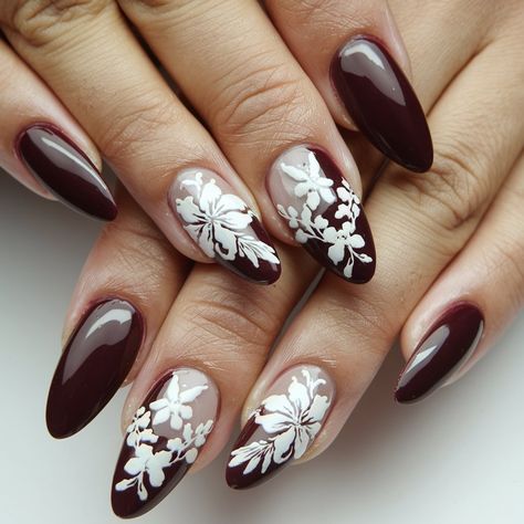 Step up your nail game with this stunning burgundy and floral design! Featuring a mix of deep burgundy and soft nude shades, the intricate white floral patterns add a touch of elegance and sophistication. Perfect for any season, this trendy almond shape manicure combines bold colors with delicate details, making it ideal for special occasions or everyday glam.  #septembernails #fallnails Burgundy Nails With Flowers, Burgundy Floral Nails, Burgundy And White Nails, Almond Shape Manicure, Burgundy Nail Art, Everyday Glam, September Nails, Burgundy Nails, Almond Shape