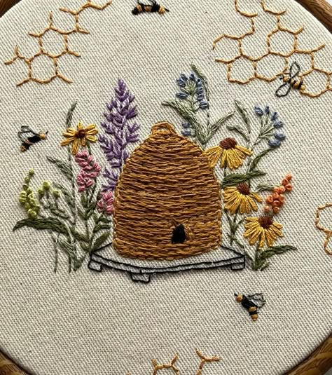 Add a touch of handmade charm to your home with this beautifully embroidered beehive hoop art. This piece features intricate hand-stitched details, including a traditional beehive surrounded by vibrant flowers and busy bees. The honeycomb patterns scattered around the hoop add a whimsical touch. Perfect for nature lovers and embroidery enthusiasts, this art piece is displayed in a wooden embroidery hoop, making it easy to hang on your wall or display on a shelf. The natural, rustic feel of this Embroidered Beehive, Honeycomb Embroidery Pattern, Bumble Bee Embroidery Pattern, Intricate Embroidery, Honey Bee Wildflowers, Beehive Embroidery, Honeycomb Embroidery, Bumble Bee Embroidery, Bee Embroidery Pattern Free