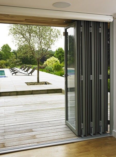 Rooms Outdoor created a contemporary poolside room in Oxfordshire with changing rooms hidden behind a cedar-clad door. The large bi-folding doors open onto the pool, and provide views of the huge garden designed by Philip Nash. Sliding Folding Doors Exterior, Outdoor Bi Folding Doors, Patio Sloding Doors, Bifold Windows, Aluminium Sliding Doors Balcony, Aluminium Bi Fold Doors, Bifolding Doors, Bifold Patio Doors, Huge Garden