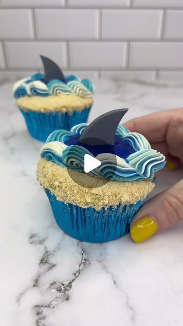 Rachel Lindsay on Instagram: "You’re gonna need a bigger boat 😛🦈

Would you take a bite of these shark week cupcakes that I made for @wiltoncakes 🦈

How to 💁🏼‍♀️🦈🧁
🌊 Cut a curved sheet of parchment paper and stick it onto the top of the cupcakes, leaving a small gap at one side.
🦈 Spread the sand-coloured buttercream over the gap.
🌊 Crush up shortbread/graham crackers into sand and pour them over the buttercream.
🦈 Peel off the parchment paper.
🌊 Use an offset spatula to add some of the blue buttercream to the centre the other side of the cupcake.
🦈 Add white, and two shades of blue buttercream to a piping bag, fitted with piping tip 32.
🌊 Pipe a shell border around one side of the cupcake.
🦈 Put them in the fridge for 20 minutes for the buttercream to set firm.
🌊 Pour a sm Seahorse Cupcakes, Cupcake Decorating Ideas For Men, Ocean Cupcakes, Shark Cakes, Buttercream Flowers Tutorial, Ocean Cake, Shark Cupcakes, Offset Spatula, 2024 Party