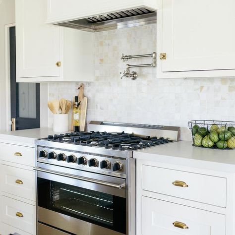 A stainless steel oven range sits between white shaker cabinets donning brass cup pulls and a white quartz countertop fixed against calcutta gold marble grid backsplash tiles. Off White Cabinets, Quartz Backsplash, Kitchen Aid Appliances, White Shaker Cabinets, Classic Kitchen, Counter Tops, Updated Kitchen, White Cabinets, New Classic