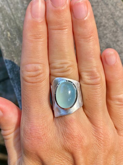 This one is a true eye catcher.  Very modern and contemporary adjustable sterling silver ring with perfect diamond aqua chalcedony cabochon.  Looks amazing and very hip on when worn.  Asymmetrical shape of ring will surely make a statement.  The wide band is of free -form adjustable design, very original, yet simple. The band is not only has a free - form wavy contour but also slightly etched to give the band a matte finish to match the chalcedony.  Very beautiful, industrial and comfortable to Long Silver Ring, Modern Oval Cabochon Jewelry With Large Stone, Modern Adjustable Oval Moonstone Ring, Modern Oval Sterling Silver Moonstone Ring, Modern Oval Moonstone Ring With Large Stone, Modern Silver Moonstone Cabochon Ring, Modern Rings With Large Oval Cabochon Stone, Handmade Oval Moonstone Ring In Modern Style, Modern Moonstone Ring With Large Stone