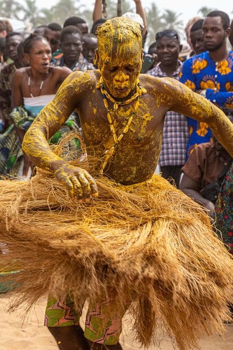 An African man in a grass skirt and covered in yellow paste dancing in front of a crowd African Tribe Aesthetic, Africa Burn Festival, African Music Aesthetic, Benin Voodoo, African Festival, West African Fantasy Aesthetic, Carnival In Rio, Galle Fort, Music Singing