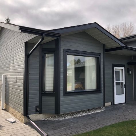 We replaced the existing steel siding with Canexel's D5 Ridgewood siding in Granite. Black LP Smart Trim borders the corners and windows, and new black fascia and eavestrough help finish this stunning transformation. Grey Siding House, Black Trim Exterior House, Outdoor House Paint, Dark Grey Houses, Grey Exterior House Colors, Hardie Board, Mobile Home Exteriors, Grey Siding, Gray House Exterior