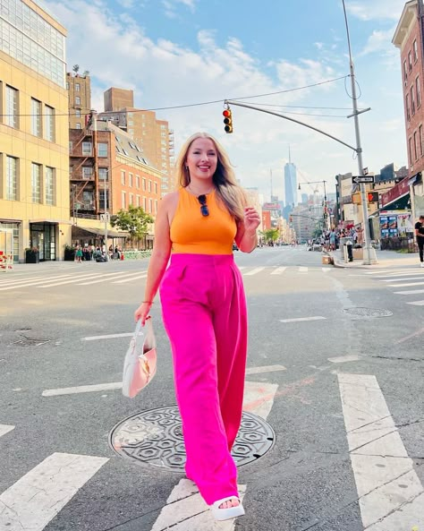 Sarah is wearing bright pink wide leg pants and an an orange top. She has a white handbag and white platform sandals. In the background you can see the One World Trade Center in the background. Downtown Brunch Outfit, Colorful Bar Outfit, Summer Outfit Inspiration Midsize, Colorful Mid Size Outfits, Colorful Summer Outfits Midsize, Colourful Outfits Midsize, Quirky Midsize Fashion, Mid Size Fashion Colorful, Bright Colored Outfits Plus Size