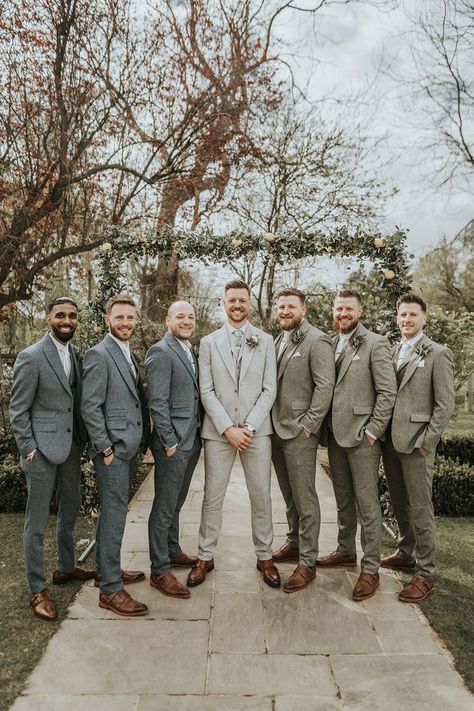 Groom in pale grey suit with mint green tie with groomsmen in blue suits and some in green suits with white flower buttonholes and brown shoes