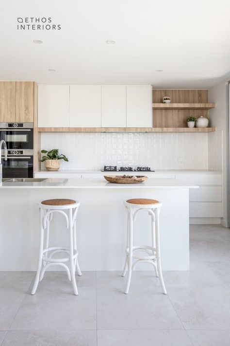 White and wood kitchen with light grey porcelain tile floors. White stone benchtops and a white square tile feature on the splashback. There are 2 white wood and rattan bar stools in front of the island bench, which holds a kitchen sink with chrome mixer. Square Textured Tile, Stone Benchtop Kitchen, White Tile Splashback, Porcelain Tile Floor Kitchen, Grey Kitchen Tiles, Modern Coastal Kitchen, Modern Kitchen Tiles, White Kitchen Lighting, White Kitchen Splashback