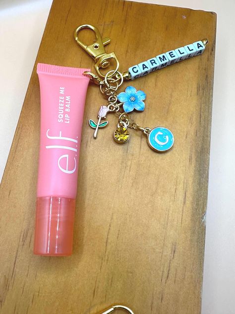 Hey, beauty lovers! Get ready to elevate your lip balm game with our Lip Balm Clip with Charms. This adorable accessory not only keeps your Elf lip balm handy but also adds a touch of personality with its cute charms. Clip it on for convenience and say goodbye to digging through your bag to find your lip balm! Perfect for on-the-go use, this charming clip ensures your lips stay moisturized wherever you are. Stay stylish and never lose your favorite lip balm again with our Lip Balm Clip with Charms! Simply select 3 charms from our options and give me the name you want on the clip! Elf Lip Gloss Keychain, Elf Lip Balm Keychain, Lip Balm Charm, Cute Gifts For Your Sister, Lip Keychain, Sister Gifts Ideas, Elf Lip Balm, Lip Balm Keychain, Pink Lip Balm