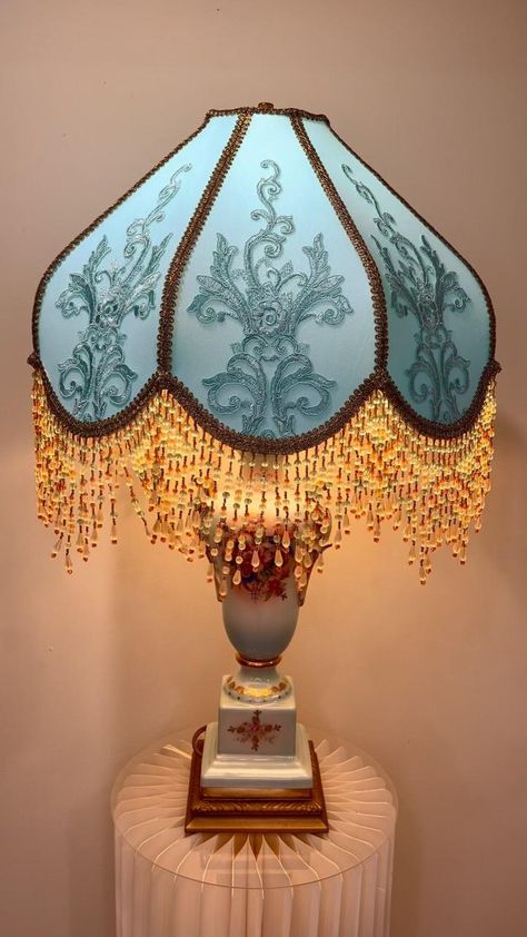 Step into the Elegance of Bridgerton ✨  This Victorian lampshade is pure enchantment—its celestial blue shade, embroidered with imported satin-thread tulle, evokes the grandeur of a bygone era. The antique porcelain base, adorned with golden arabesques and delicate birds, brings timeless sophistication, while the golden and blue beaded fringe dances with the light, casting a warm, romantic glow.  More than just a lamp, it’s a piece of history, a touch of Regency-era glamour for your home. Wou... Old Lamp Shades, Make A Lamp, Victorian Lampshades, Celestial Blue, Bygone Era, Regency Era, Creative Stuff, Gothic Beauty, Beaded Fringe