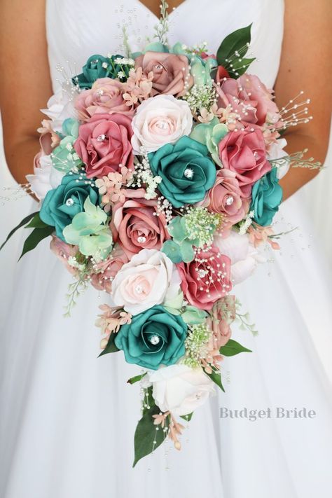 This brides’ bouquet is the perfect option if you have chosen a classic theme for your wedding. A lovely array of dusty rose and mauve are center-stage in this stunning arrangement. This bouquet is made with dusty rose-colored roses, mauve roses, barely pink roses and teal roses all accented by pearls and rhinestones. As always, this bouquet has been wired by hand and designed by our in-house florists - you can rest assured that our bouquets will maintain their quality and stand the test of time Teal And Blush Pink Wedding, Teal Pink And Gold Wedding, Teal And Coral Wedding Ideas, Pink And Turquoise Wedding Decorations, Teal And Pink Wedding Bouquet, Pink And Turquoise Wedding Theme, Rose Gold And Teal Wedding Theme, Coral And Teal Wedding Bouquet, Rose Gold And Turquoise Wedding Theme