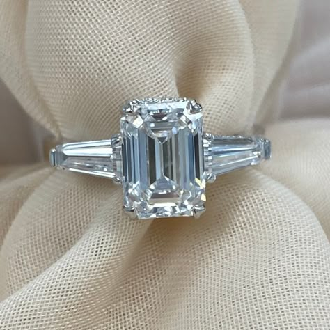 This stunning three stone engagement ring features a 2.05 carat center emerald cut lab grown diamond flanked by two baguette side lab grown diamonds. The center diamond is set in a prong setting that allows the light to fully penetrate the stone, showcasing its brilliance and fire. The baguette side diamonds add a touch of elegance and sophistication to the ring.  This ring is the perfect way to show your loved one how much you care. It is a timeless and elegant piece of jewelry that they will cherish for years to come. The ring comes with International Gemological Institute Certificate (IGI) # LG620463552 Metal - 14k White Gold Metal Weight - 3.1g Total Carat Weight - 3.23 Width Top/Width Shank - 9.7 x 6.4/2.4 mm Center Stone - 2.05 Carat D Color VVS2 Clarity Emerald Cut Lab Grown Diamond Emerald And Baguette Engagement Ring, Emerald Cut Ring With Baguettes, Timeless White Gold Emerald Ring With Baguette Cut, Emerald Baguette Cut Ring In Diamond White, 3 Carat Emerald Diamond Ring, Emerald Cut With Baguettes, Wedding Emerald Ring In 14k White Gold, Baguette Cut, Diamond White Emerald Ring, Baguette Cut, Baguette-cut Emerald Ring With Diamond Accents