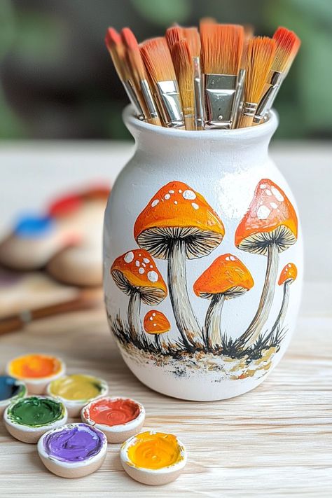 A painted pottery vase featuring orange mushrooms with brushes and colorful paint, ideal for cottagecore-themed decor. Painting Mushrooms Ideas, Mushroom Pottery Painting, Mushroom Painting Ideas, Mushroom Pottery, Painting Mushrooms, Pottery Painting Ideas Easy, Painted Pottery Ideas, Cottage Core Art, Plain Mugs