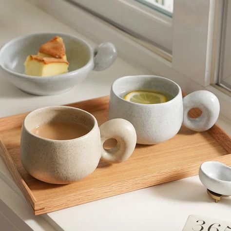 Funky and organic looking ceramic glazed mugs not only add retro decor to your home, but they create cozy moments out of the simplicity of drinking your favorite beverages. The handcrafted nature, glazing, and kiln processes preformed on the pottery ensures each cup has its own character with exaggerated handle design—adding to their natural appearance and organic retro style. Available in two different earthy colors and organic shapes offering two options of shallow and deep sizes for sipping, Japanese Stoneware, Cute Coffee Cups, Beige Ceramic, Cerámica Ideas, Retro Coffee, Neutral Aesthetic, Tableware Design, Modern Japanese, Nordic Home