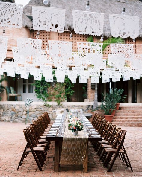 Karen Ruezga and her team at Villa Amor created an elegant reception space, set with two long tables decorated with gold-striped runners, small floral centerpieces, and candles. Hanging overhead were swags of bistro bulbs and delicate papel picado (Mexican paper cut) flags. The color palette was based off of nature—using plants, flowers, sand, and sunsets as the main inspiration. Papel Picado Wedding, Wedding Flags, Mexican Themed Weddings, Hacienda Wedding, Blended Families, Wedding Reception Seating, Boda Mexicana, Destination Wedding Mexico, Wedding Venues Beach