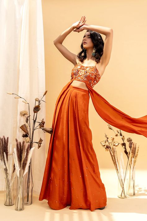 Editor's Note Floral Embroidery V-neck Blouse With Asymmetrical Side Drapes And Single Pleated Crystals Embellished High Waist Pant Color: Rust Orange Fabric: Crepe, Tulle Net, Shantoon Embroid... Orange Indian Outfit, Daytime Glam, Haldi Outfits, Floral Frocks, Embroidered Pants, Indian Bridal Outfits, Designer Dresses Casual, Top And Pants Set, Indian Wedding Outfits