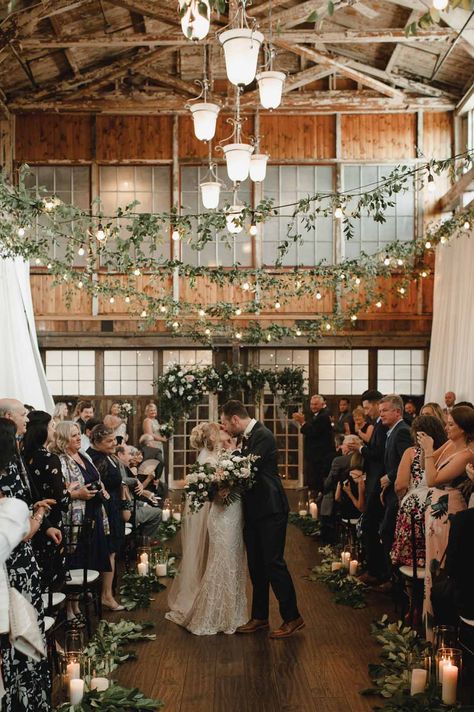 Cafe Lights Wedding, Pew Flowers, Bride And Groom Kissing, Ceremony Candles, Wedding Color Pallet, Ceremony Aisle, Brewery Wedding, Green Vines, Romantic Backdrop