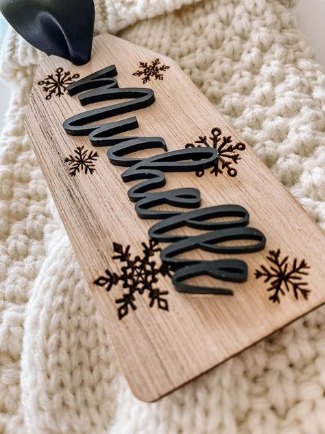 "- Personalized Wooden Stocking Name Tag -  This stocking tag is beautiful, chic and the perfect addition to your Christmas stocking.   This stocking tag is made of 1/8\" birch and measures 2.5\" wide x 5.5\" long.  A beautiful 1.5\" wide satin ribbon has been added for easy hanging and fray check has been added to prevent fraying.    The name has been laser cut and is made of 1/8\" acrylic.  The background of the tag has snowflakes that have been laser engraved into the wood." Easy Glowforge Projects, Holiday Laser Projects, Laser Made Gifts, Wooden Laser Crafts, Christmas Stocking Name Tag Ideas, Cricut Christmas Stockings, Laser Cnc Projects, Cricut Stocking Tags, Laser Business Ideas